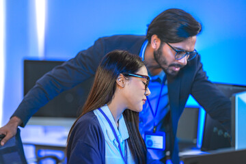 Asian female AI programmer and Indian male data analyst reviewing code on a monitor. Diverse tech...