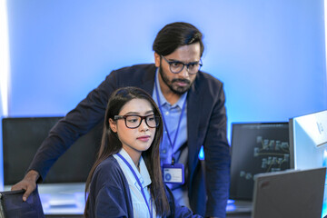 Asian female AI programmer and Indian male data analyst reviewing code on a monitor. Diverse tech...