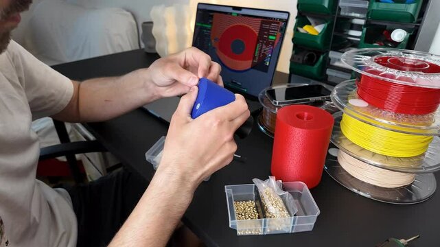 A person engages in 3D printing, showcasing technology, innovation, and creativity Caucasian male adult includes filament spools and a laptop