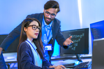Asian female AI programmer and Indian male data analyst reviewing code on a monitor. Diverse tech...