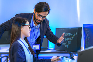Asian female AI programmer and Indian male data analyst reviewing code on a monitor. Diverse tech...