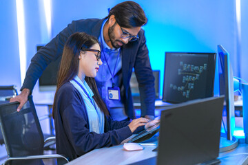 Asian female AI programmer and Indian male data analyst reviewing code on a monitor. Diverse tech...