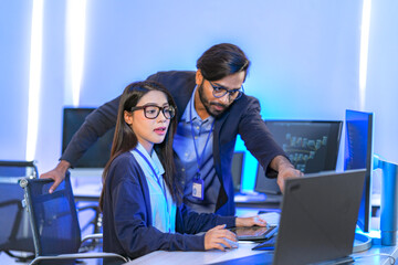 Asian female AI programmer and Indian male data analyst reviewing code on a monitor. Diverse tech...