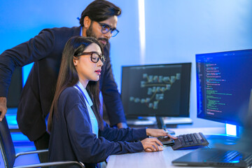 Asian female AI programmer and Indian male data analyst reviewing code on a monitor. Diverse tech...
