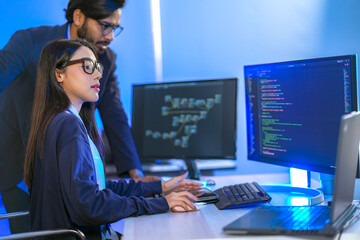 Asian female AI programmer and Indian male data analyst reviewing code on a monitor. Diverse tech...