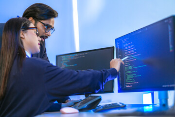 Asian female AI programmer and Indian male data analyst reviewing code on a monitor. Diverse tech...