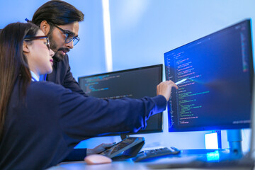 Asian female AI programmer and Indian male data analyst reviewing code on a monitor. Diverse tech...