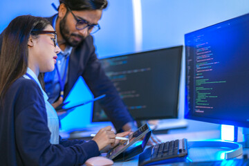 Asian female AI programmer and Indian male data analyst reviewing code on a monitor. Diverse tech...