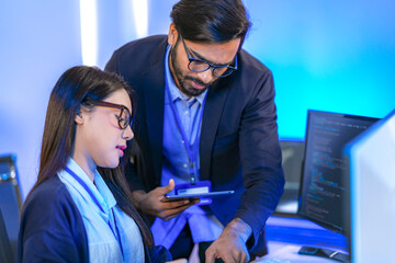 Asian female AI programmer and Indian male data analyst reviewing code on a monitor. Diverse tech...