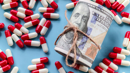 Rolled US Dollar Bills and Red and White Capsules on Blue Background