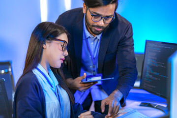 Asian female AI programmer and Indian male data analyst reviewing code on a monitor. Diverse tech...