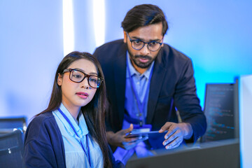 Asian female AI programmer and Indian male data analyst reviewing code on a monitor. Diverse tech...