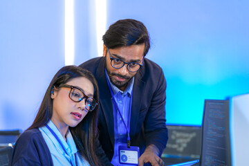 Asian female AI programmer and Indian male data analyst reviewing code on a monitor. Diverse tech...