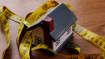 Miniature House Wrapped in Measuring Tape on Wooden Table