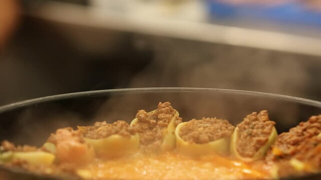 Chef stirs seasoned minced meat. Stuffed pasta shells with meat filling simmer in bubbling tomato sauce. This hearty, delicious Italian meal is perfect for a family dinner.