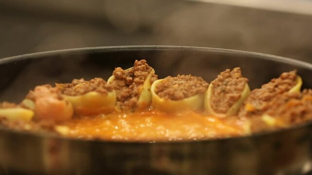 Chef stirs seasoned minced meat. Stuffed pasta shells with meat filling simmer in bubbling tomato sauce. This hearty, delicious Italian meal is perfect for a family dinner.