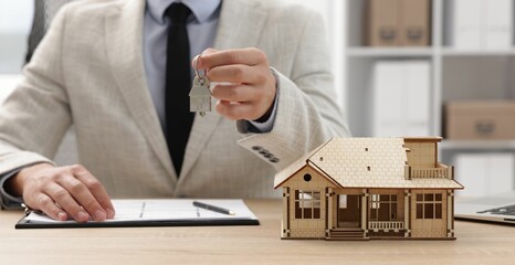 Real estate agent holding key at desk in office, focus on house model