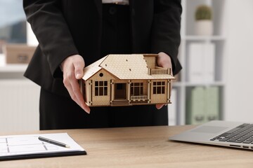 Real estate agent holding house model at desk in office, closeup