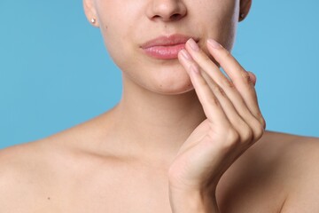 Young woman with lip balm on her lips against light blue background, closeup