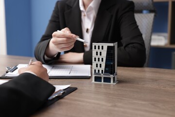 Real estate agent and client at desk in office, focus on house model
