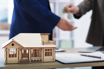 Real estate agent giving key to client at desk in office, focus on house model