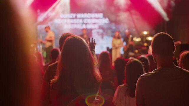 Calm worship scene with people standing, singing in soft light, and blurred musicians and lyrics on stage in the background. Ideal for faith content, church visuals, or peaceful spiritual gatherings