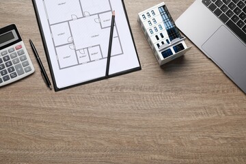 Real estate. Apartment building model, floor plan, calculator and laptop on wooden table, flat lay....