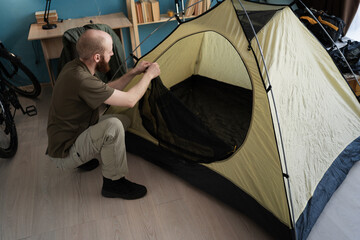 Preparing for a hike in the mountains. Packing a tent for camping at home. Bearded man hiker...