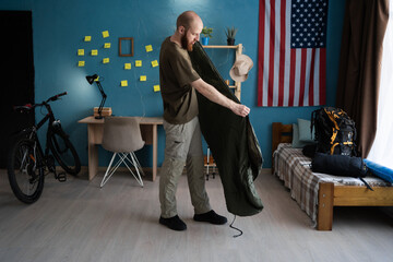 Packing for a mountain hike. Bearded traveler packing a sleeping bag for a hiking trip at home