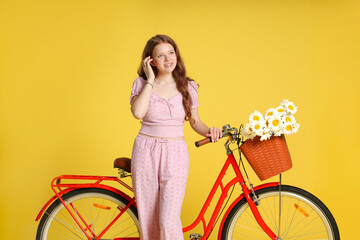 Smiling teenage girl and bicycle with basket of flowers against yellow background