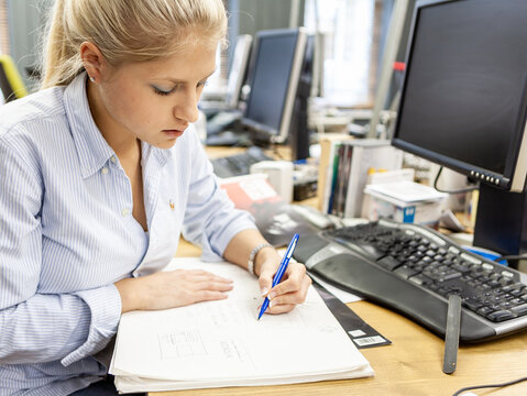 The Media Agency: Writing Notes. A female media professional researching her project at her desk in the office. From a series of related images.
