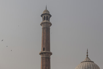 View of a minaret and dome of a mosque piercing the sky, with birds dotting the misty air, showcasing the architectural majesty, New Delhi, Delhi Division, India.