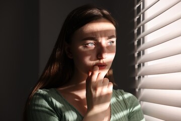 Paranoia. Worried woman near window at home