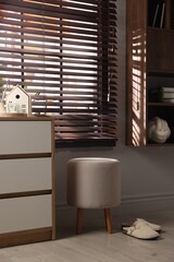Stylish pouf and slippers near chest of drawers at home