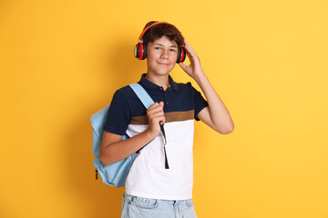 Teenage boy in headphones with backpack on orange background