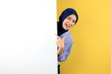 A Joyful Asian Woman in Blue Navy Hijab and Striped Shirt Excitedly Points at a Blank White Board