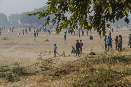Agra, India - 24 June 2025: View of a dusty field teeming with children playing cricket under a hazy sky, the stark contrast of youthful energy against the muted landscape.