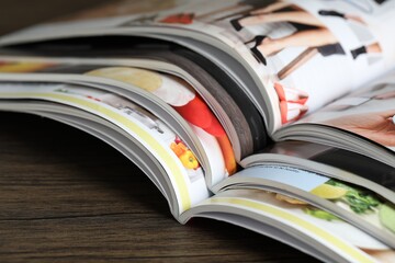 Different open magazines on wooden table, closeup