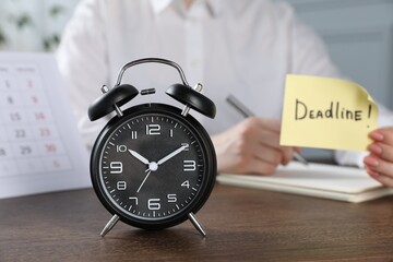 Woman holding sticky note with word Deadline while writing notes at wooden table in office, focus...