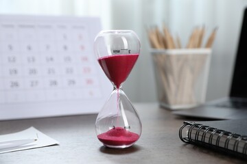 Deadline. Hourglass with flowing sand, stationery, calendar and laptop on wooden table indoors