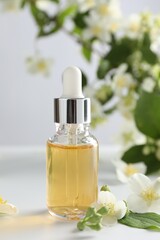 Essential oil and beautiful jasmine flowers on white table, closeup