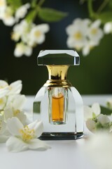 Bottle of perfume and jasmine flowers on white table against blurred background, closeup