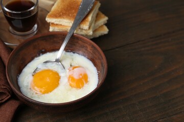 Traditional asian breakfast with half-boiled eggs in bowl, soy sauce and toasted bread on wooden table, closeup. Space for text