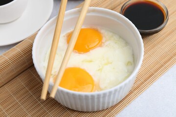Half-boiled eggs in bowl, soy sauce and chopsticks on light grey table, closeup. Traditional asian breakfast