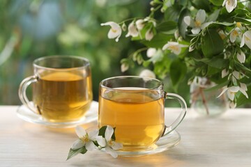 Tasty jasmine tea in cups and flowers at white wooden table, closeup