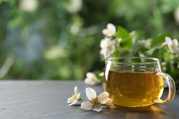Tasty jasmine tea in cup and flowers on black table, closeup. Space for text