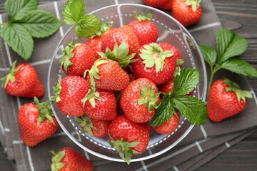 Fresh ripe strawberries and leaves in container on black wooden table, flat lay