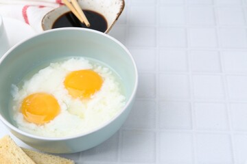 Traditional asian breakfast with half-boiled eggs in bowl, soy sauce, bread and chopsticks on white tiled table, closeup. Space for text