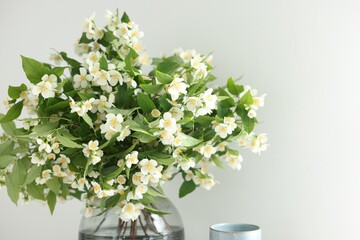 Beautiful jasmine flowers in vase near white wall indoors, closeup. Space for text