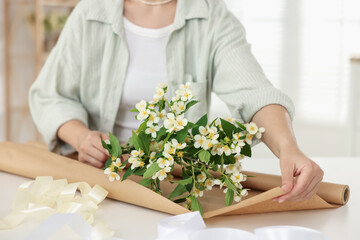 Woman making bouquet of jasmine branches at white table, closeup